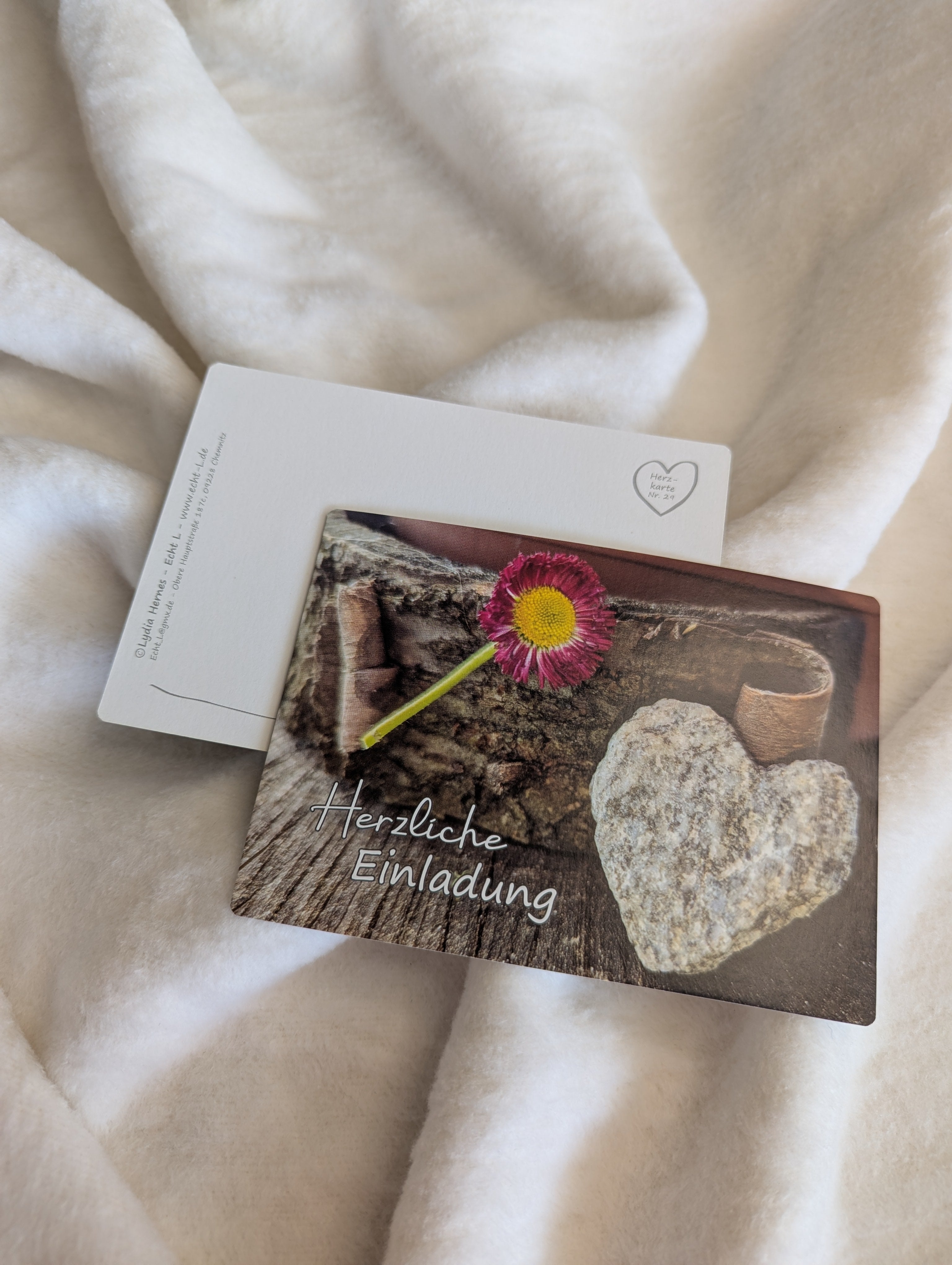 Postkarte Herzliche Einladung – Naturherz aus Stein mit rosa Gänseblümchen auf Holz